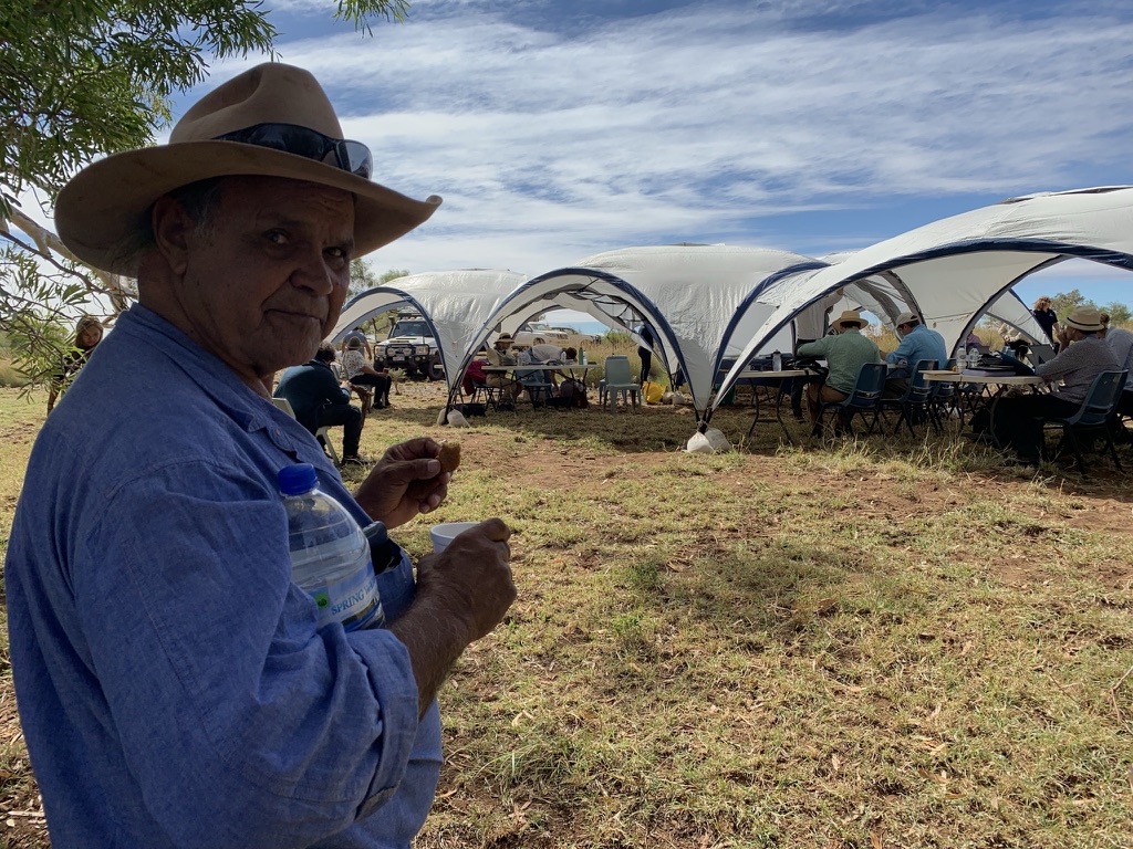 A person standing in front of tents with people seating at tables under the tents.