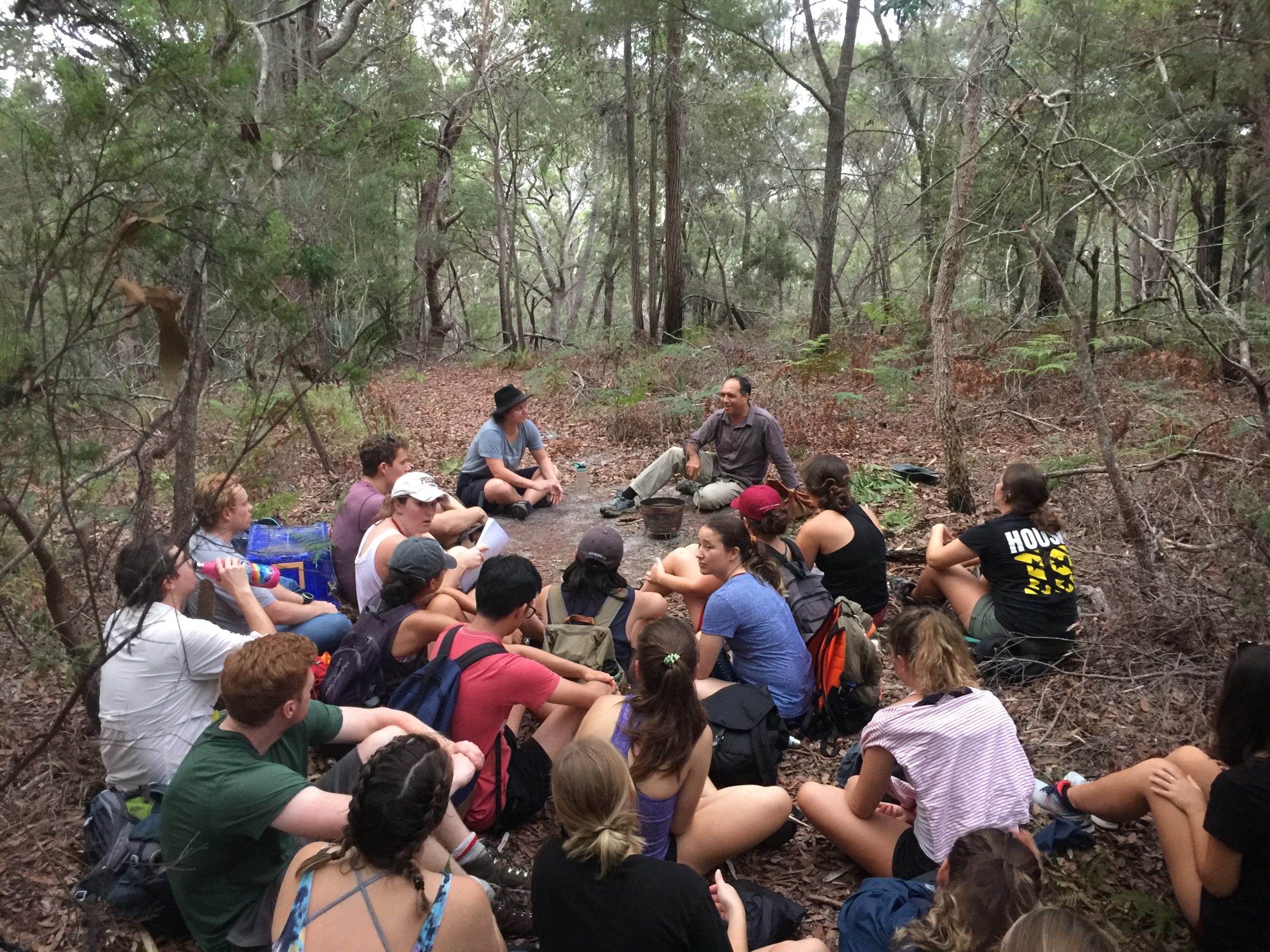 Group of students sitting on the ground in the bush with the Traditional Owners.
