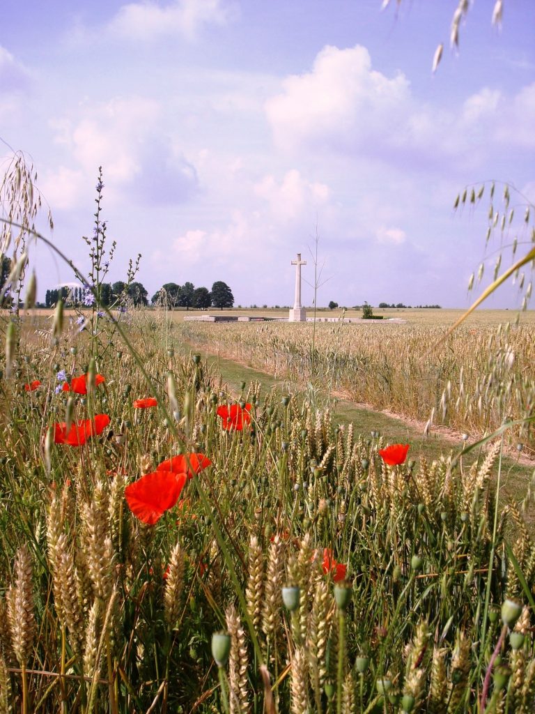 Depicts a small military cemetery near the Bullecourt battlefield of 1917, with the Remembrance cross in the background, and red poppies in foreground