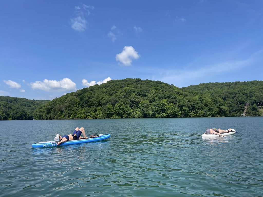 Blue lake with two White women lying down on their paddle board under a blue sky.