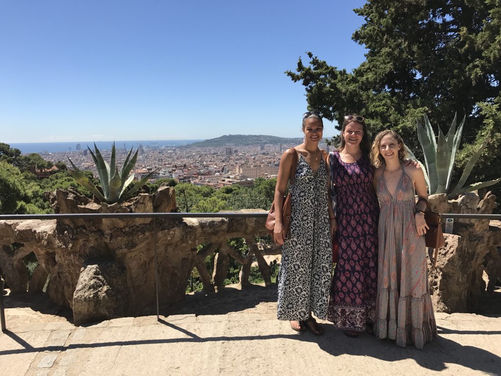 Three women in long dresses posing for the camera with a cityscape backdrop of Barcelona