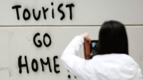 A person taking a photo of graffiti which reads 'tourist go home'
