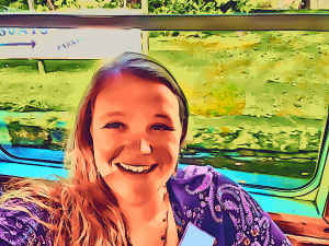 blonde smiling woman in a blue and purple paisley dress inside a canal boat in front of a window