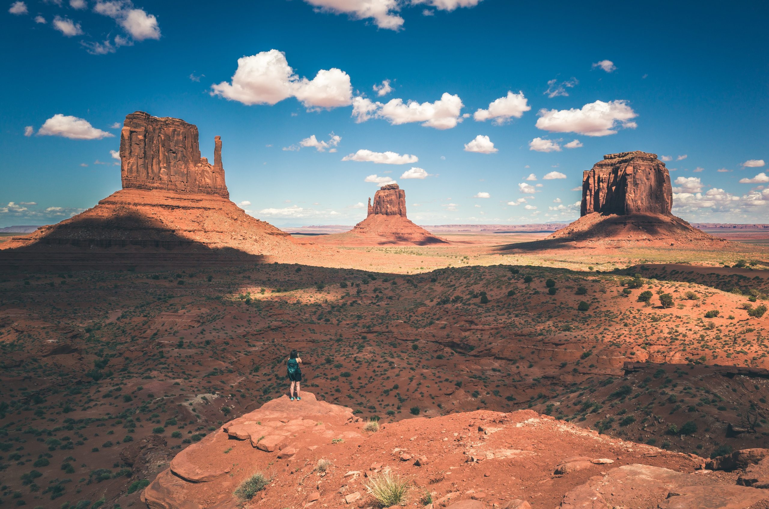 Hiker stands on top of peak looking at three sandstone buttes in the distance