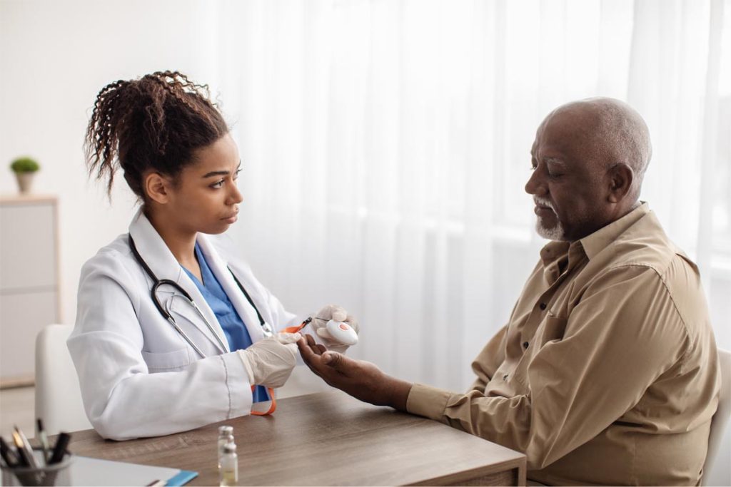 Medical worker holding personal alarm button and giving it to mature patient, sitting at table in office, explaining how to use medical alert